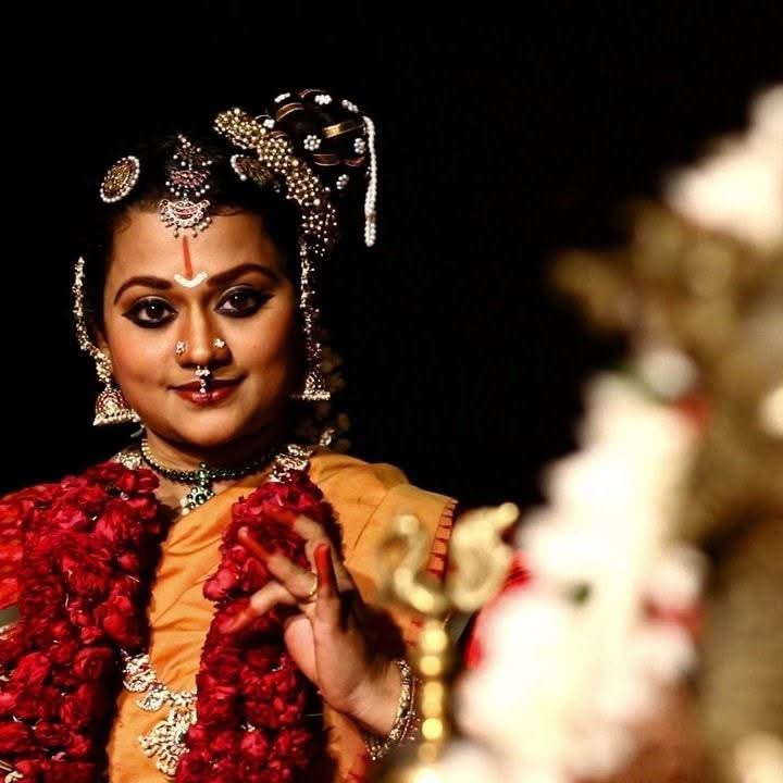 Dancer in orange and gold costume with a red flower garland, mid-gesture
