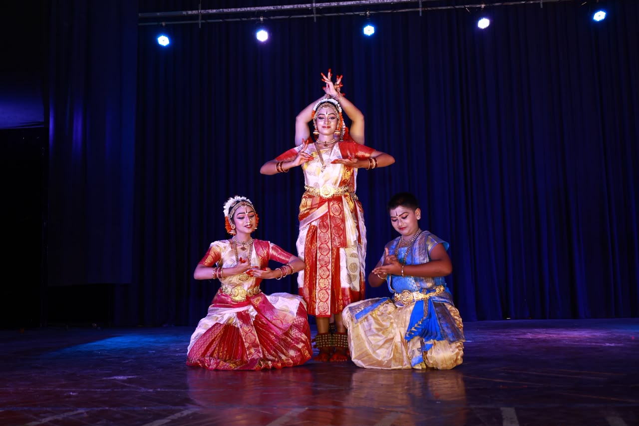 Three dancers in a formation pose on a dark stage