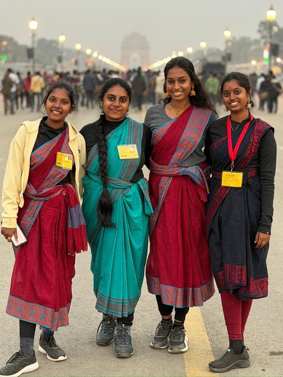 Four students in colourful sarees with parade contingent badges, India Gate in the background